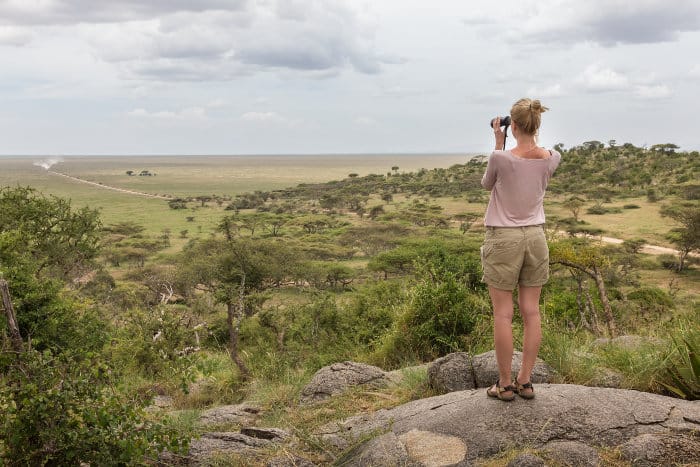 Female tourist scans the horizon with binoculars to spot African animals
