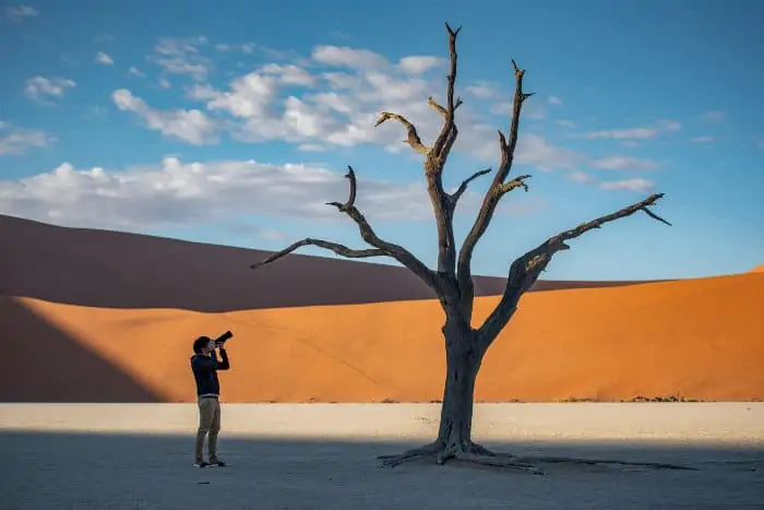 Young man taking a picture of a dead tree in Deadvlei area, Namibia