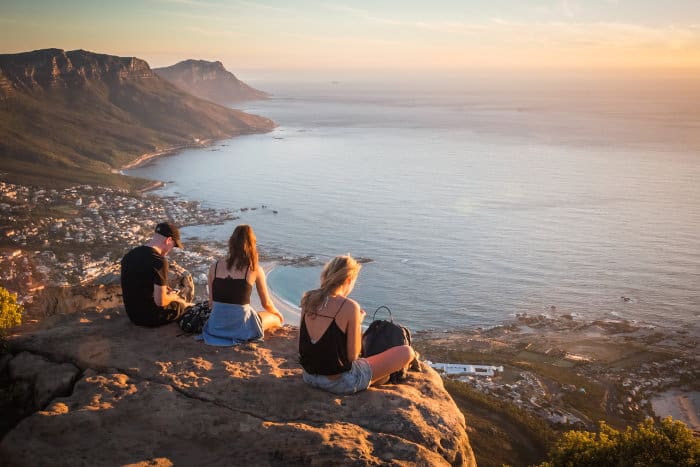 Man and women sitting on top of Lion's Head, overlooking the Atlantic Ocean and Cape Town city below