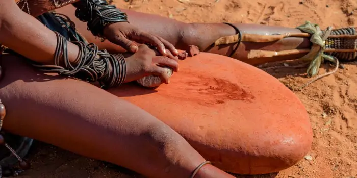 Himba woman preparing otjize, ground up ochre pigment mixed with butterfat