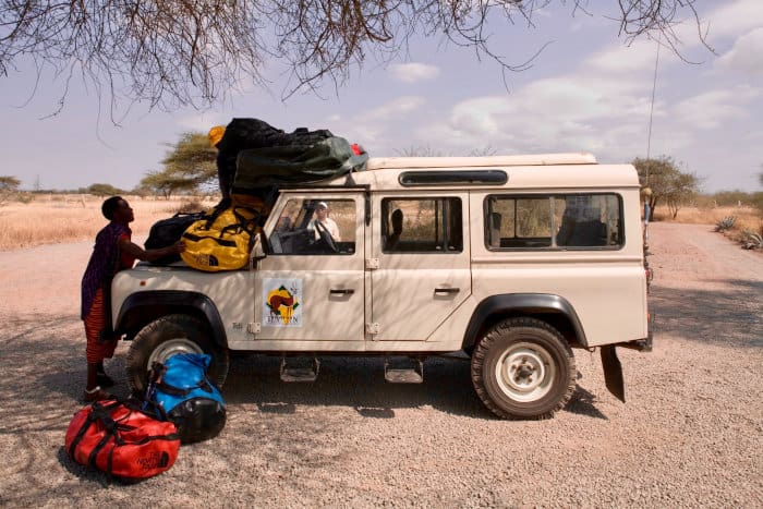 Driver loads safari luggage on top of a jeep