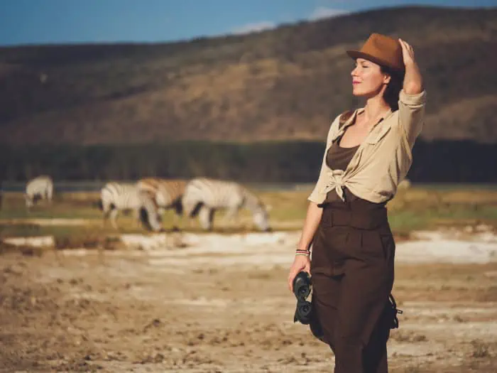 Woman in safari clothes enjoying the sun, with herd of zebra in the background
